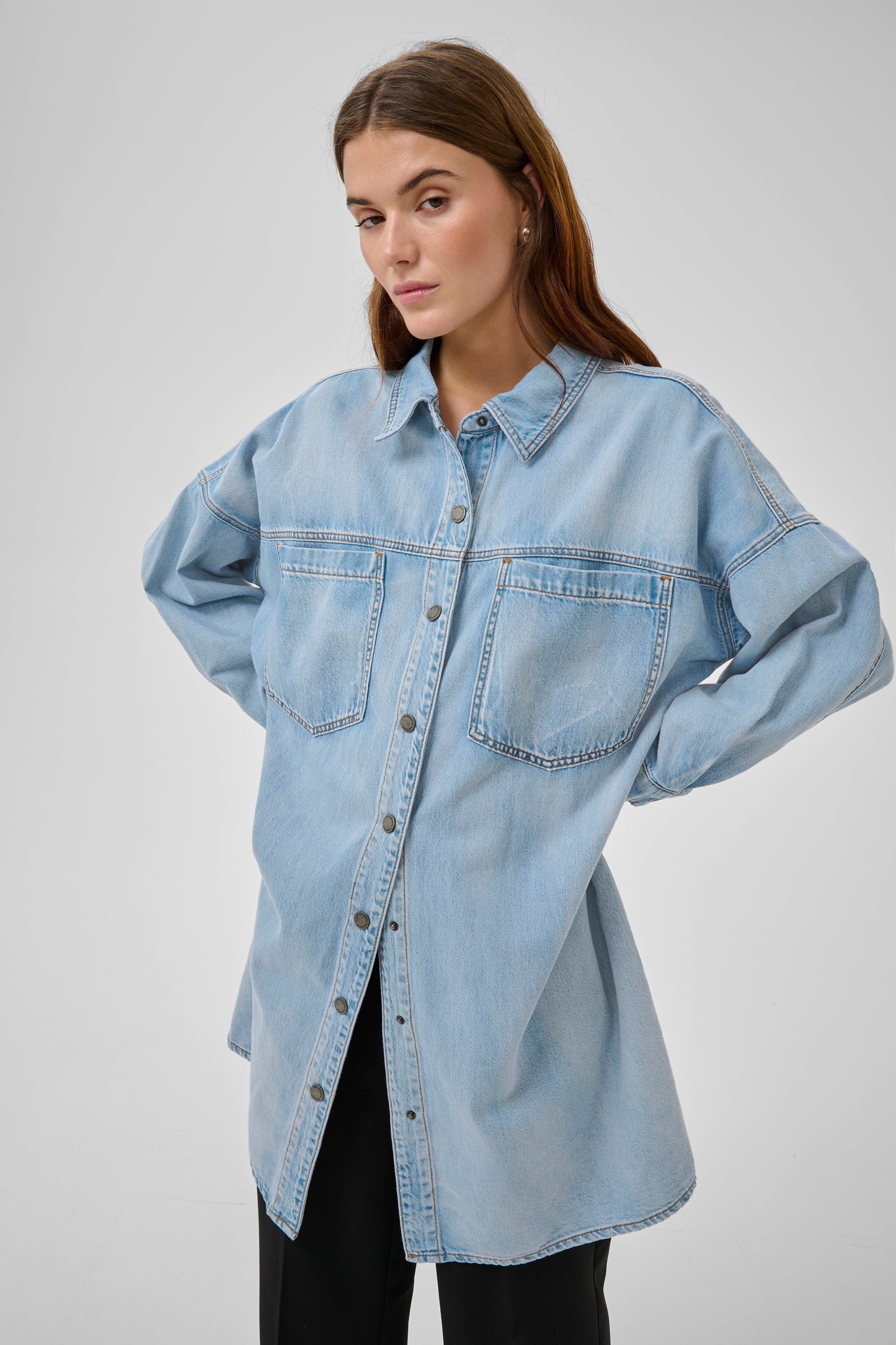 Woman wearing a light blue denim shirt against a plain background