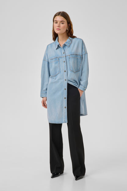 Woman wearing a light blue denim shirt over a black outfit on a white background