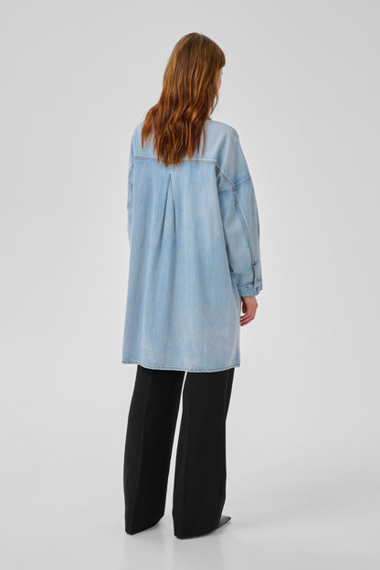 Person wearing a light blue denim shirt and black pants on a white background