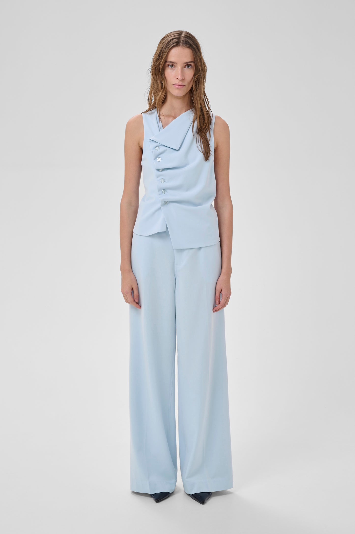 Woman wearing a light blue sleeveless top and wide-leg pants on a white background