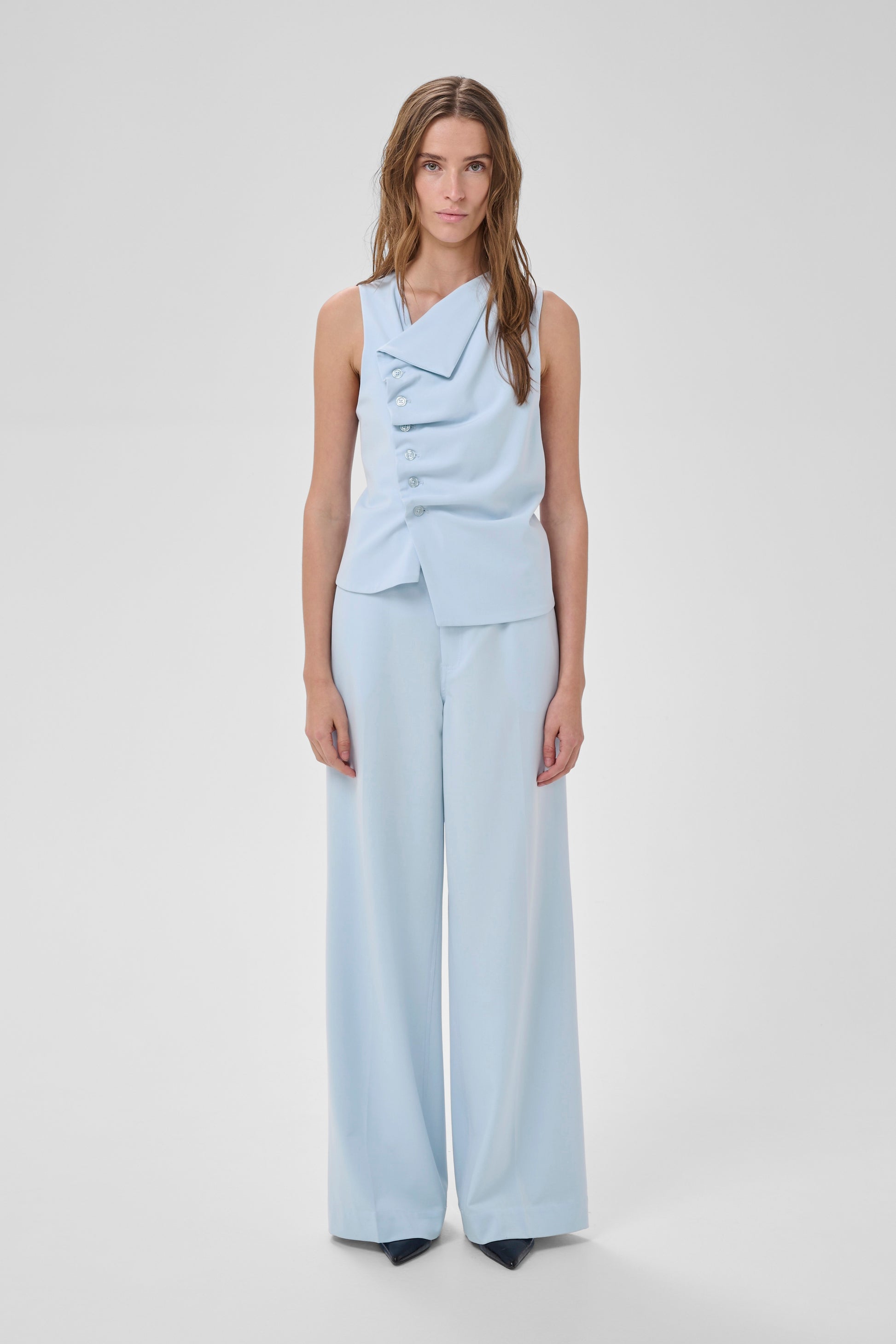 Woman wearing a light blue sleeveless top and wide-leg pants on a white background