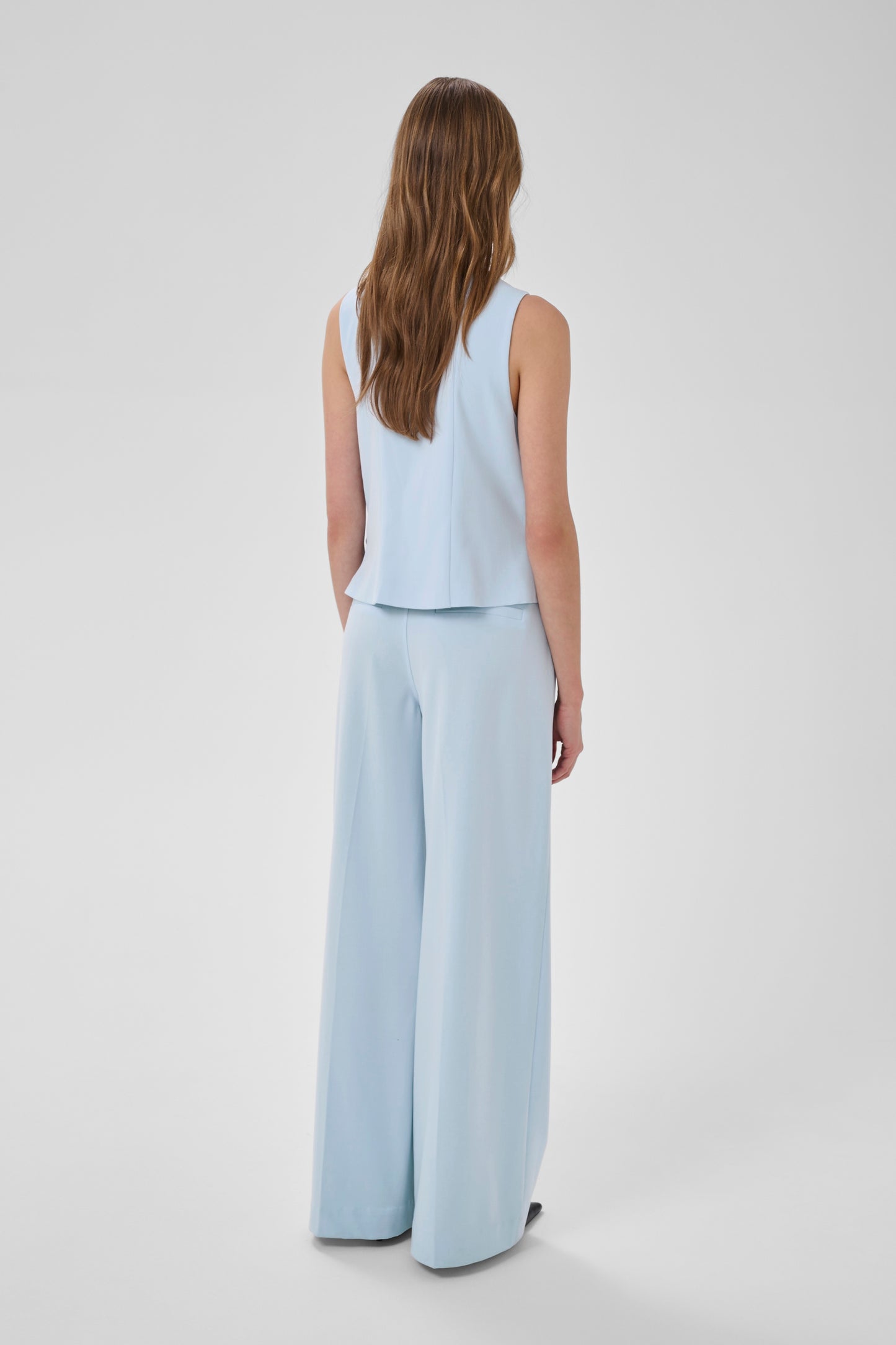 Woman wearing a light blue sleeveless top and wide-leg pants on a white background
