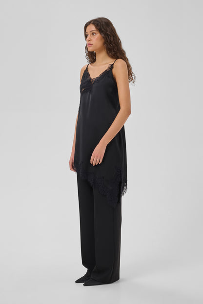 A woman modeling a black satin camisole top with lace trim and matching wide-leg trousers against a light gray studio background.