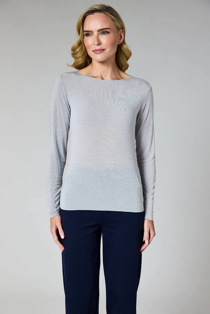 A woman modeling a light gray long-sleeve knit top with a boat neckline, paired with dark navy pants, against a neutral gray studio background.