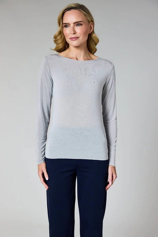 A woman modeling a light gray long-sleeve knit top with a boat neckline, paired with dark navy pants, against a neutral gray studio background.