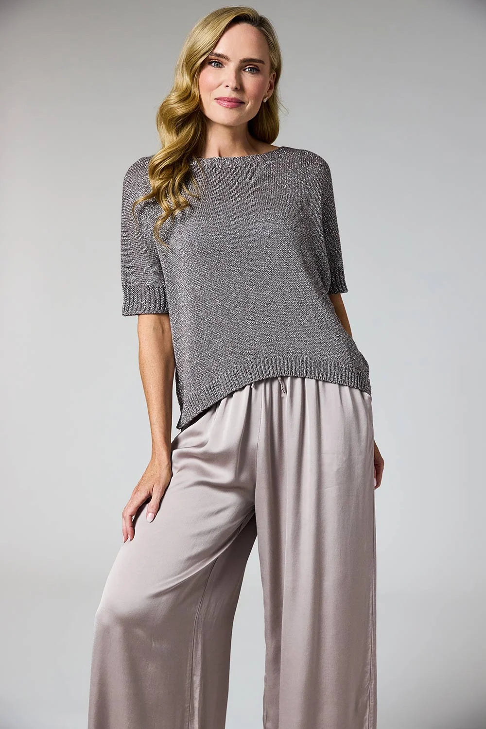A woman modeling a short-sleeve knit top in heather gray with matching gray trousers, photographed against a plain light gray studio background.