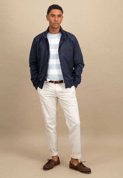 Man wearing a navy jacket, striped shirt, white pants, and brown shoes on a beige background