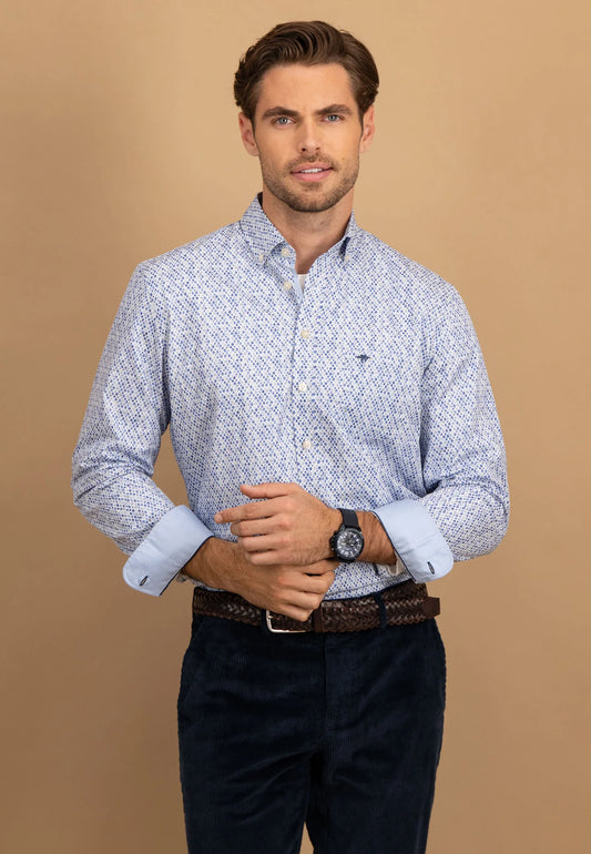 Man wearing a patterned shirt and dark pants against a beige background