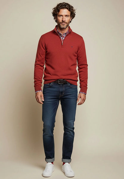 Man wearing a red sweater, blue jeans, and white sneakers against a beige background