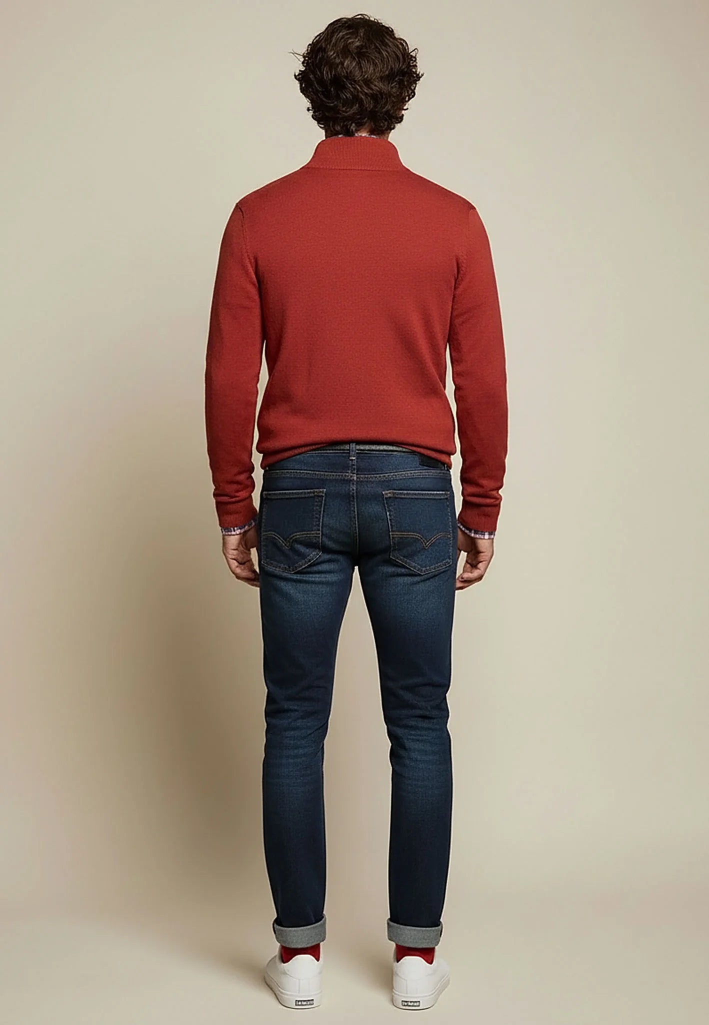 Person wearing a red sweater and dark jeans on a beige background