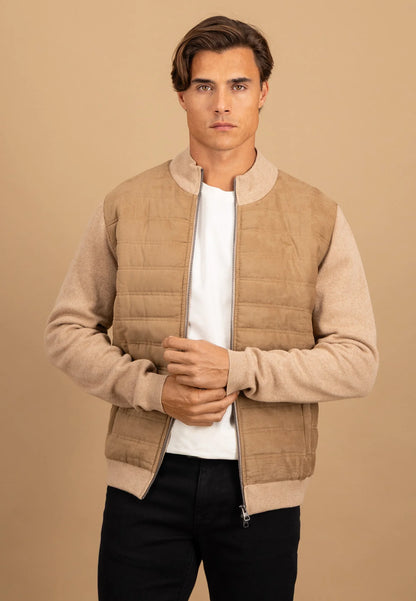 Man wearing a beige quilted vest over a white shirt and black pants on a beige background