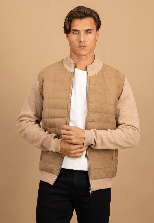 Man wearing a beige quilted vest over a white shirt and black pants on a beige background