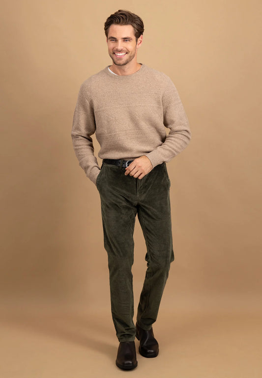 Man wearing a beige sweater and green pants against a brown background