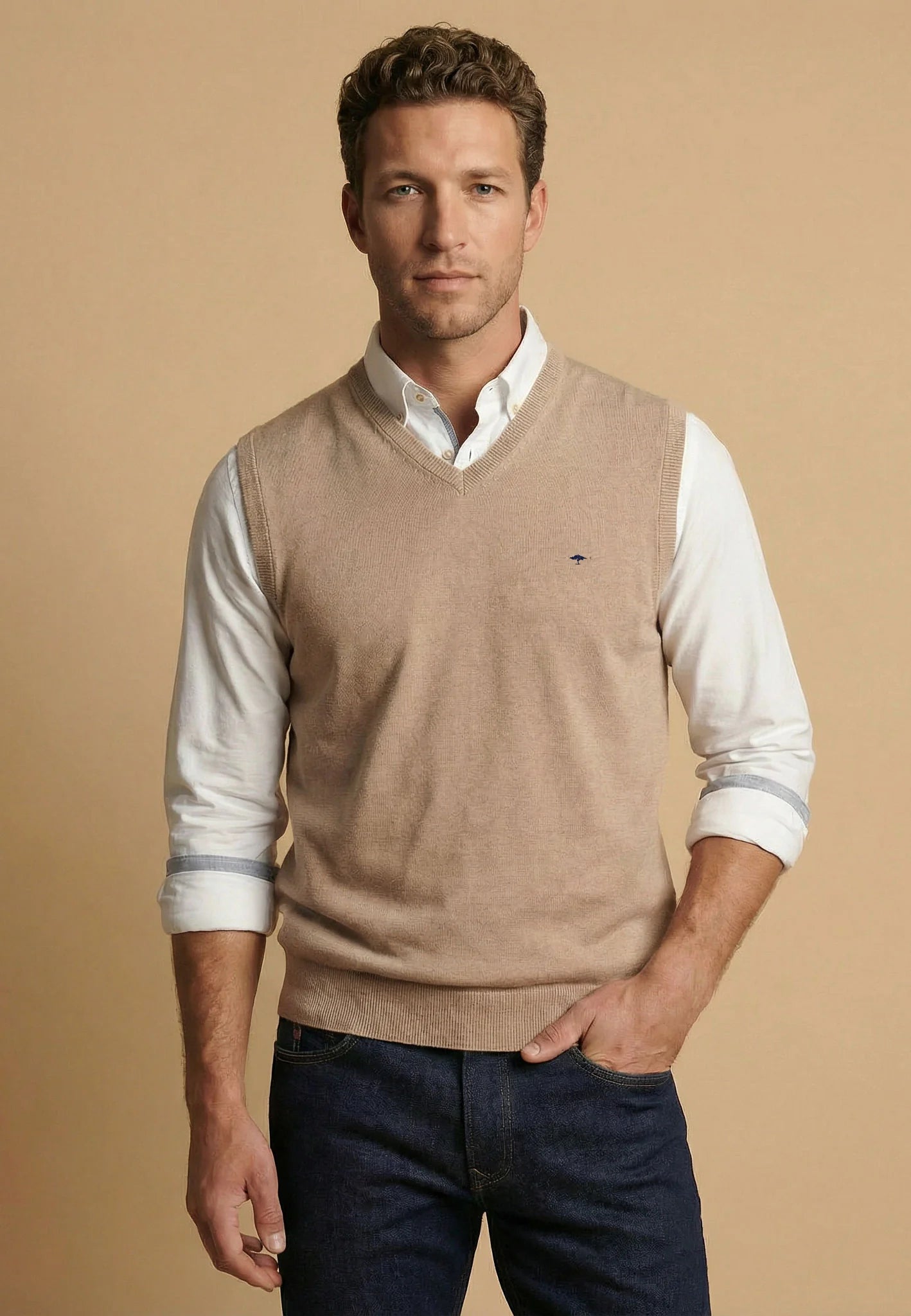 Man wearing a beige sweater vest over a white shirt with a brown background