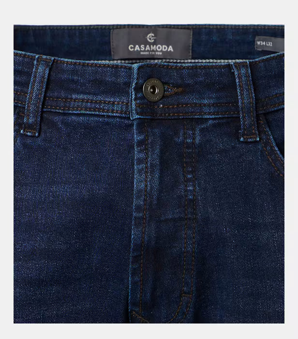 Close-up of dark blue denim jeans showing the waistband, button closure, belt loops, and front fly. The brand label reads CASAMODA.
