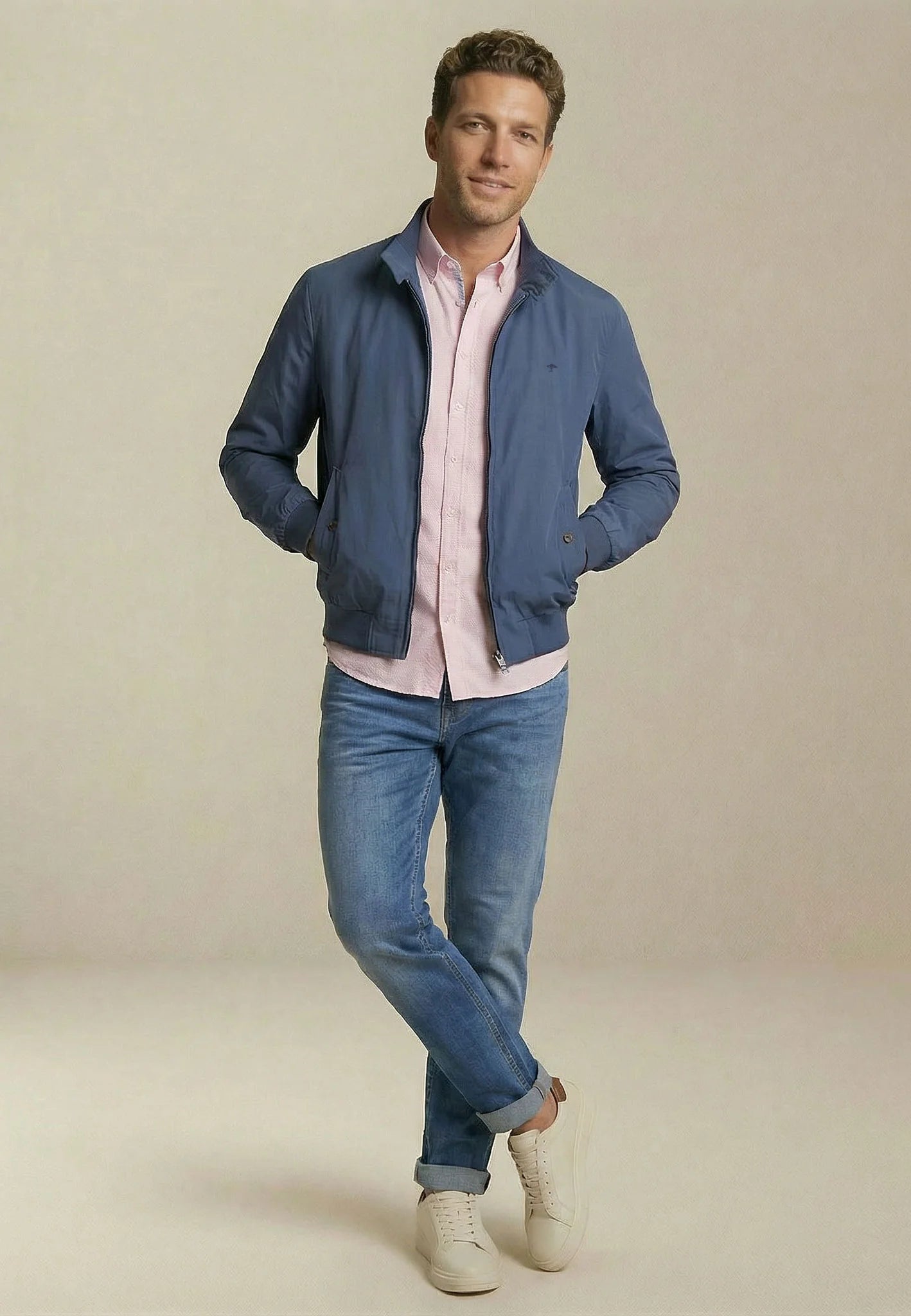 Man posing wearing blue bomber jacket,pink shirt and blue jeans with a plain background