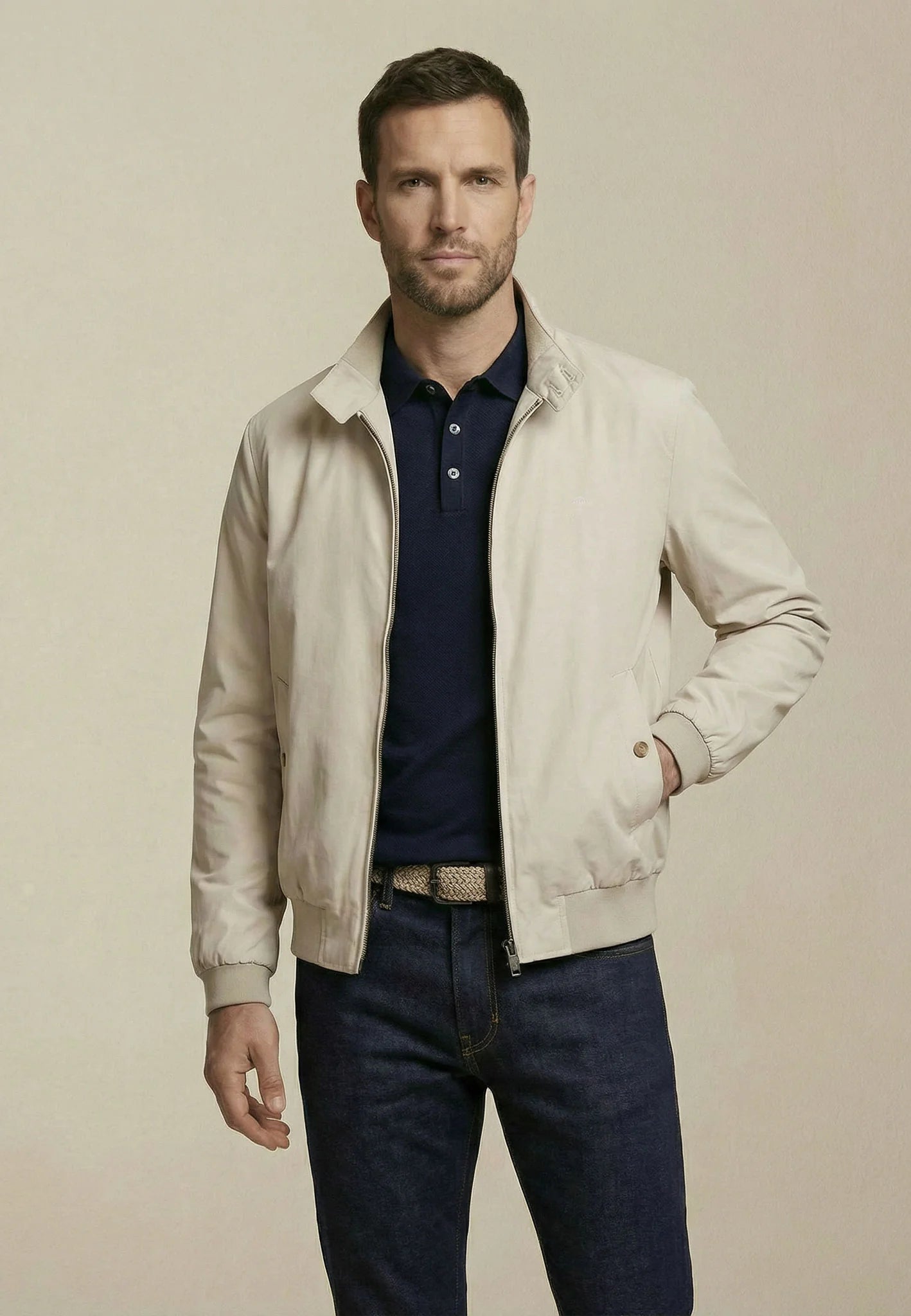 Man wearing a beige jacket over a blue shirt and jeans on a beige background