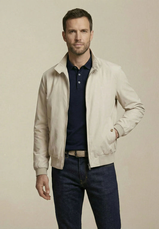 Man wearing a beige jacket over a blue shirt and jeans on a beige background