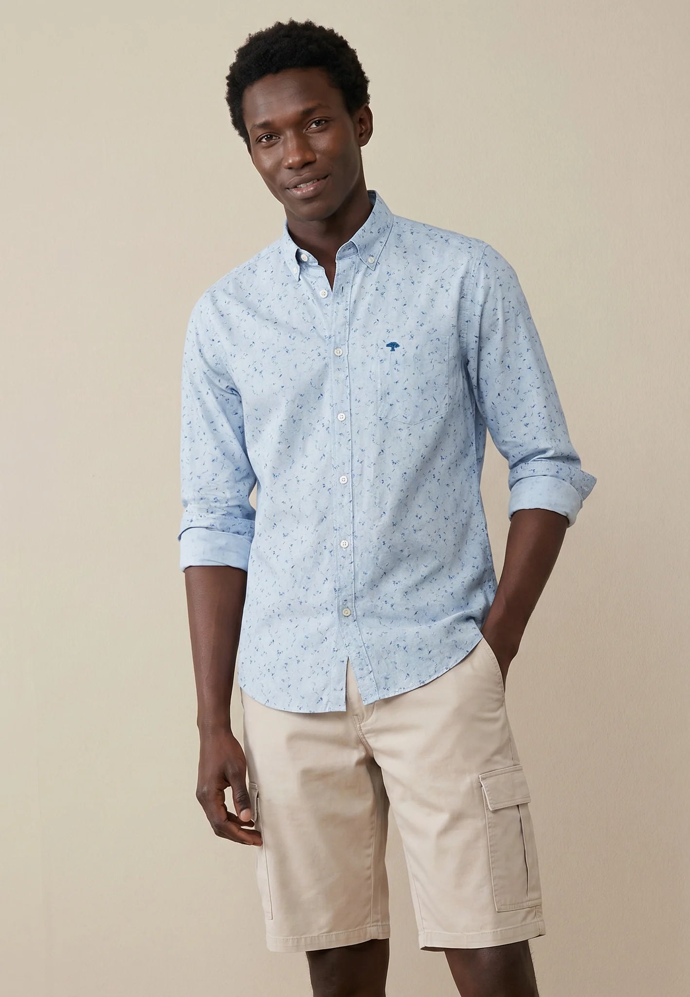Man wearing a light blue patterned shirt and beige shorts on a beige background