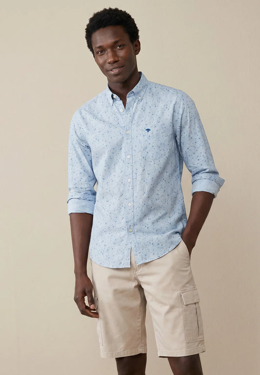 Man wearing a light blue patterned shirt and beige shorts on a beige background
