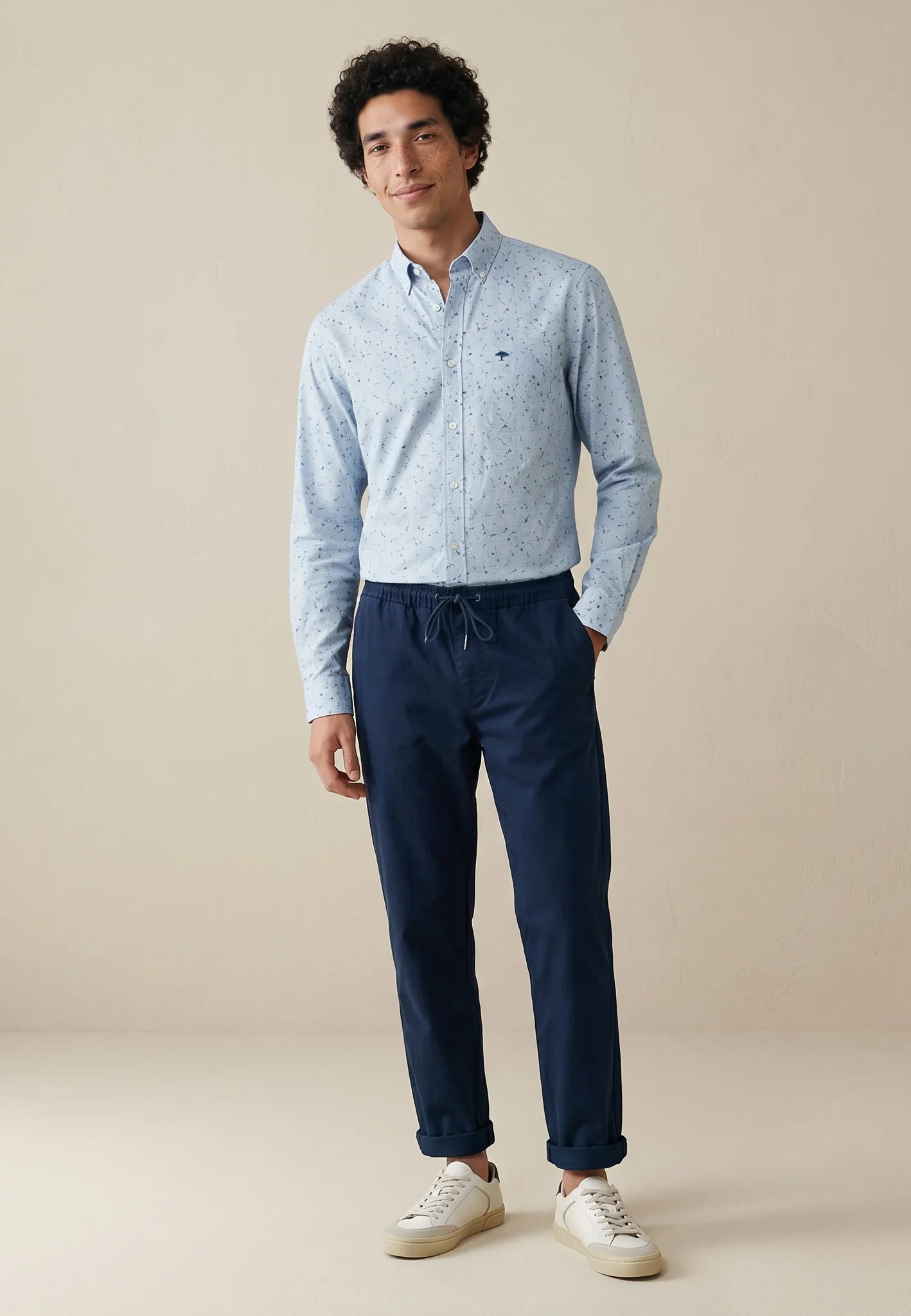 Man wearing a light blue shirt and dark blue pants on a beige background