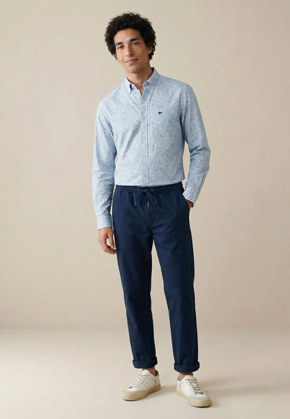 Man wearing a light blue shirt and dark blue pants on a beige background