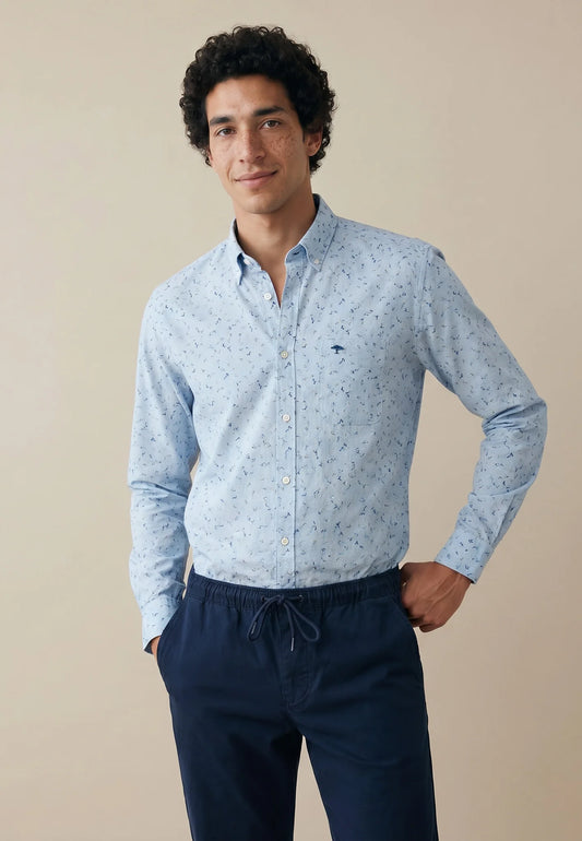 Man wearing a light blue patterned shirt and dark blue pants against a beige background