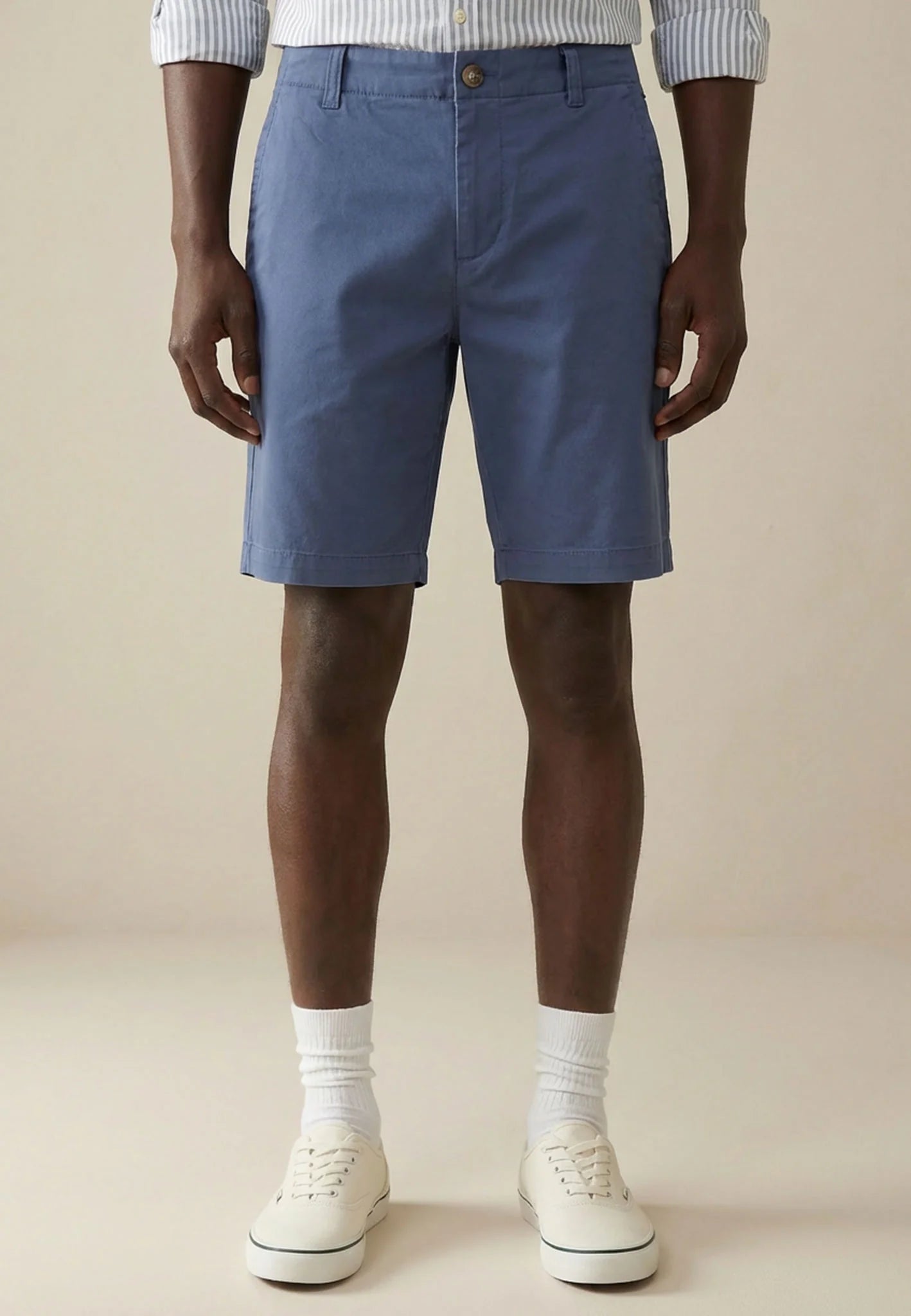 Person wearing blue shorts and white sneakers on a beige background