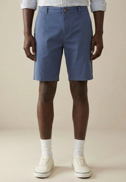 Person wearing blue shorts and white sneakers on a beige background