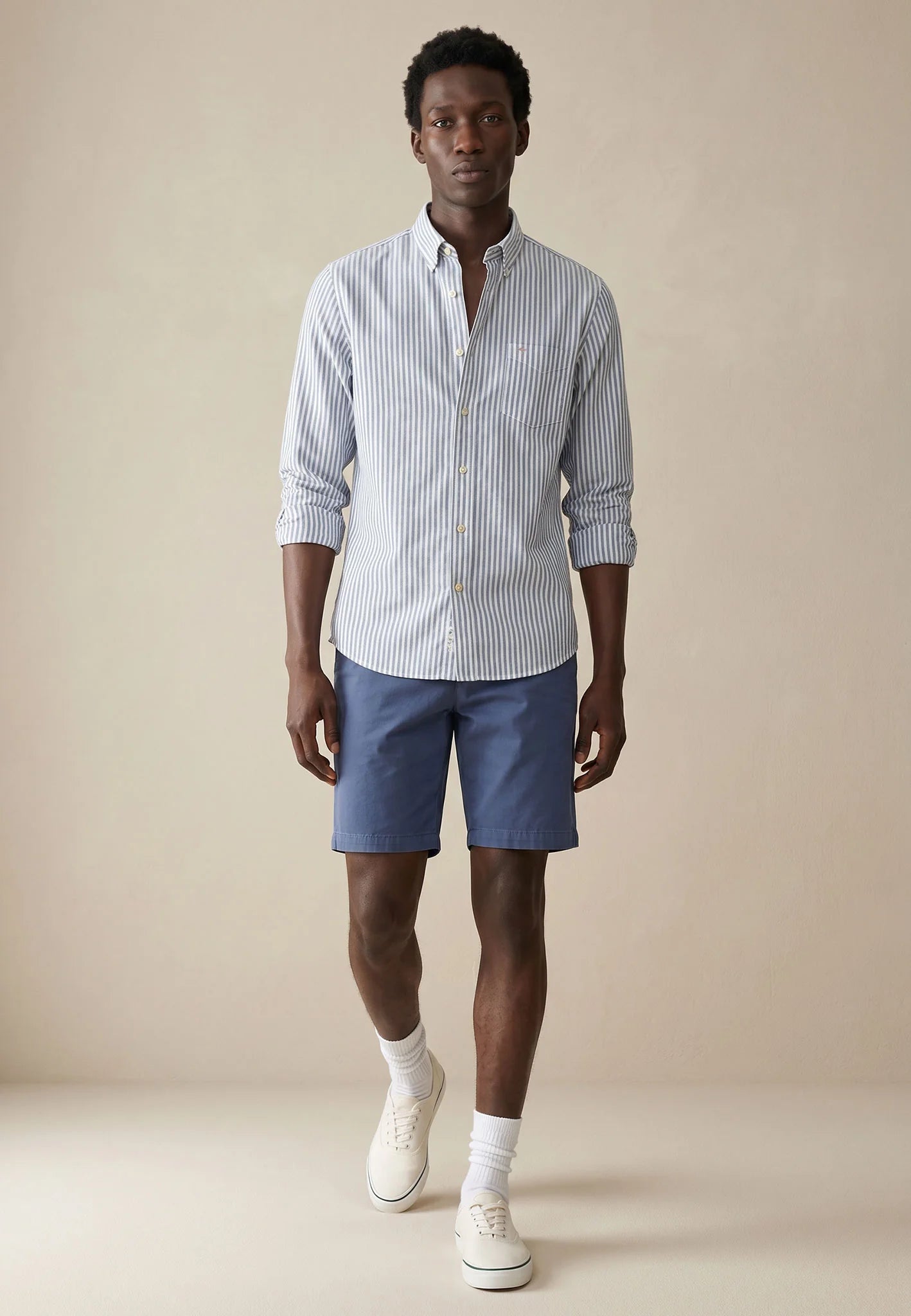 Man wearing a striped shirt and blue shorts against a beige background