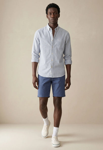 Man wearing a striped shirt and blue shorts against a beige background