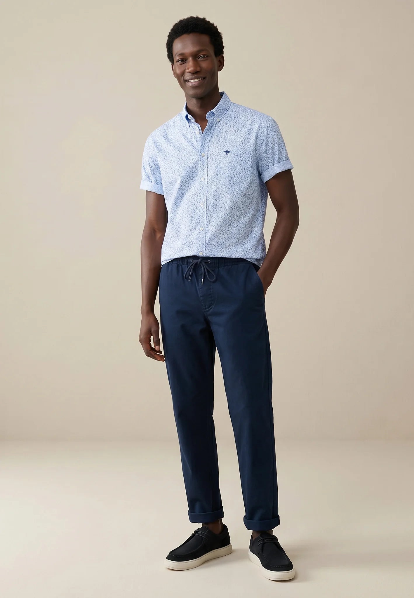 Man wearing a light blue patterned shirt and navy pants on a beige background