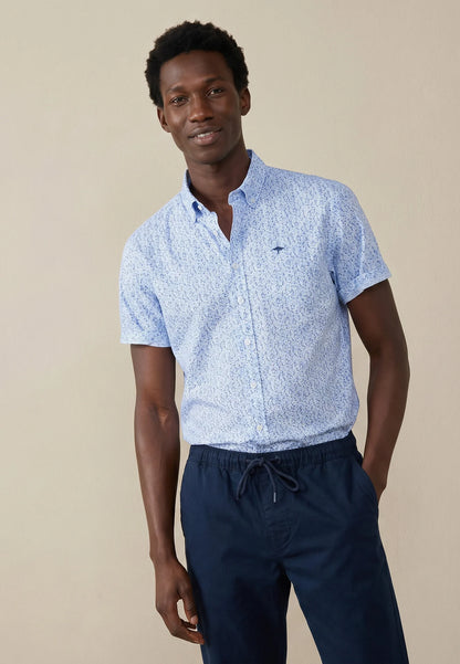 Man wearing a light blue patterned shirt and navy pants against a beige background