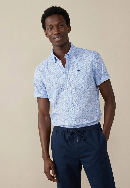 Man wearing a light blue patterned shirt and navy pants against a beige background