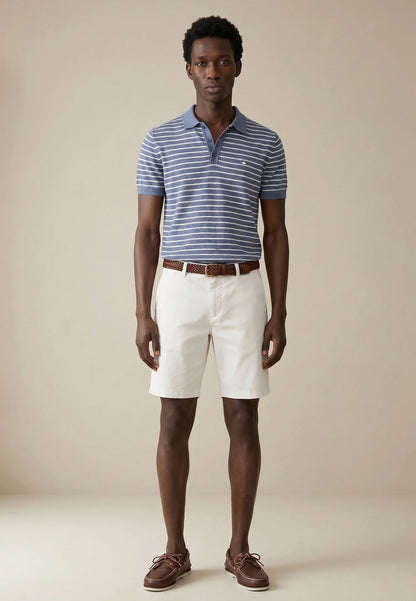 Man wearing a striped polo shirt, white shorts, and brown shoes on a beige background