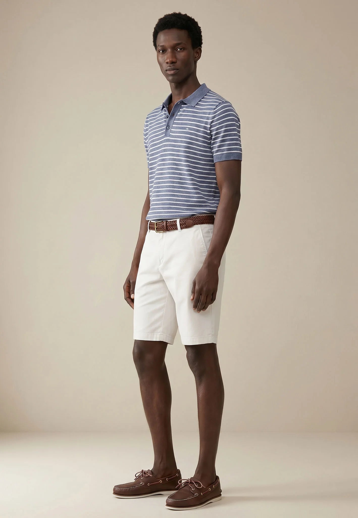 Man wearing a striped polo shirt, white shorts, and brown shoes on a beige background