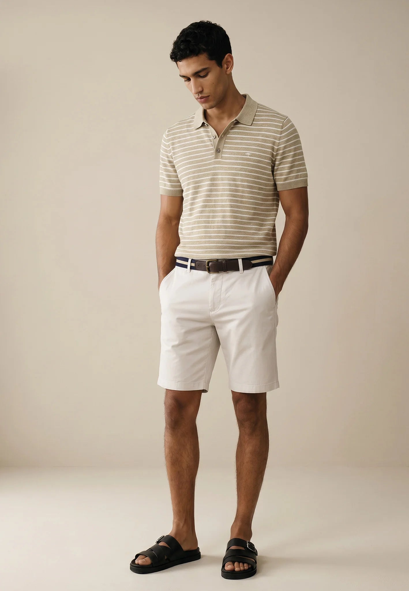Man wearing a striped polo shirt and white shorts against a beige background