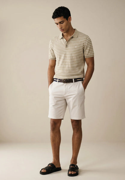 Man wearing a striped polo shirt and white shorts against a beige background