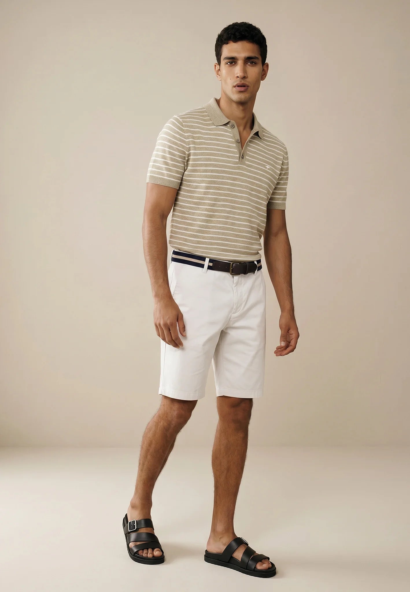 Man wearing a striped polo shirt and white shorts on a beige background