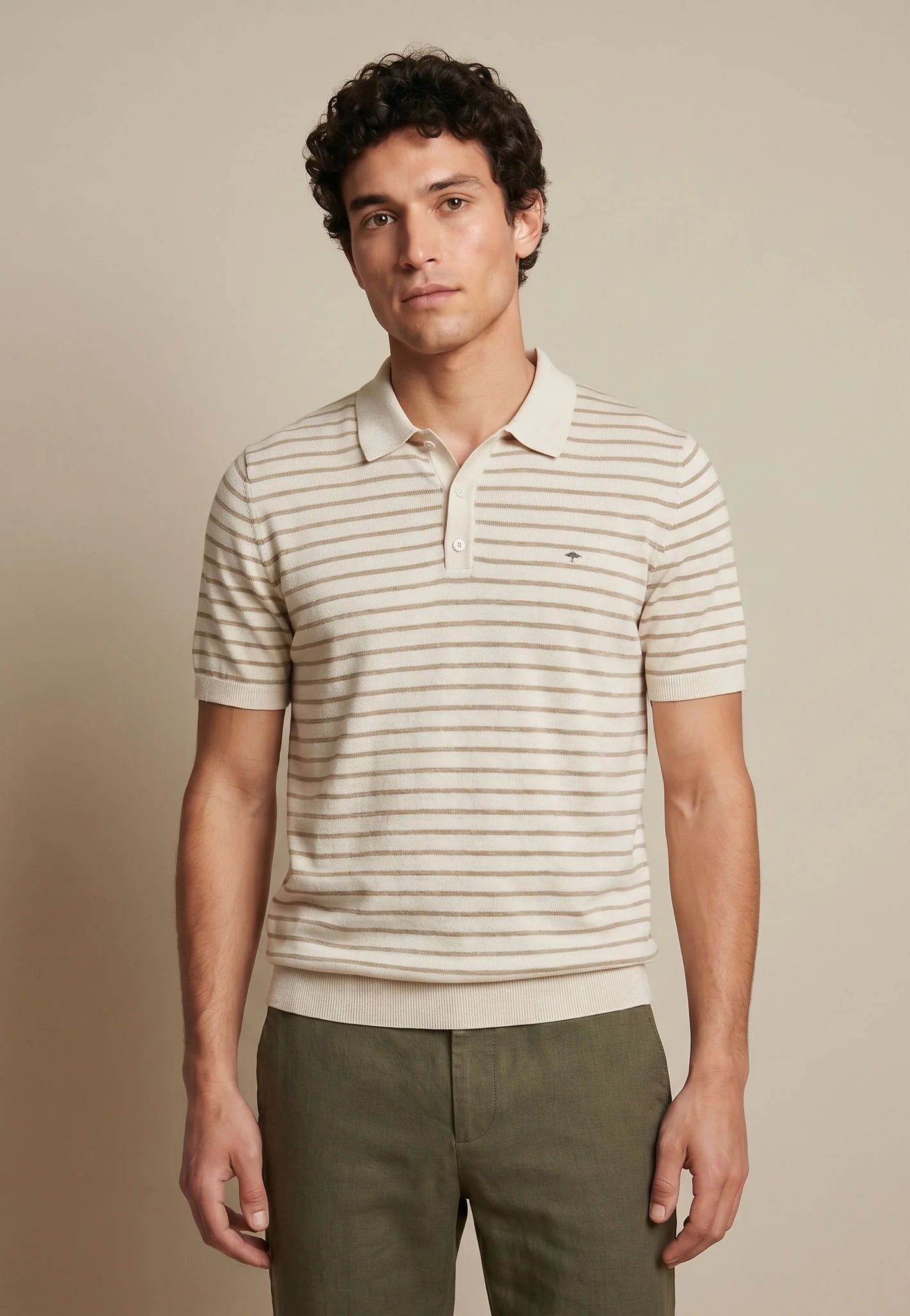 Man wearing a striped polo shirt and green pants against a beige background