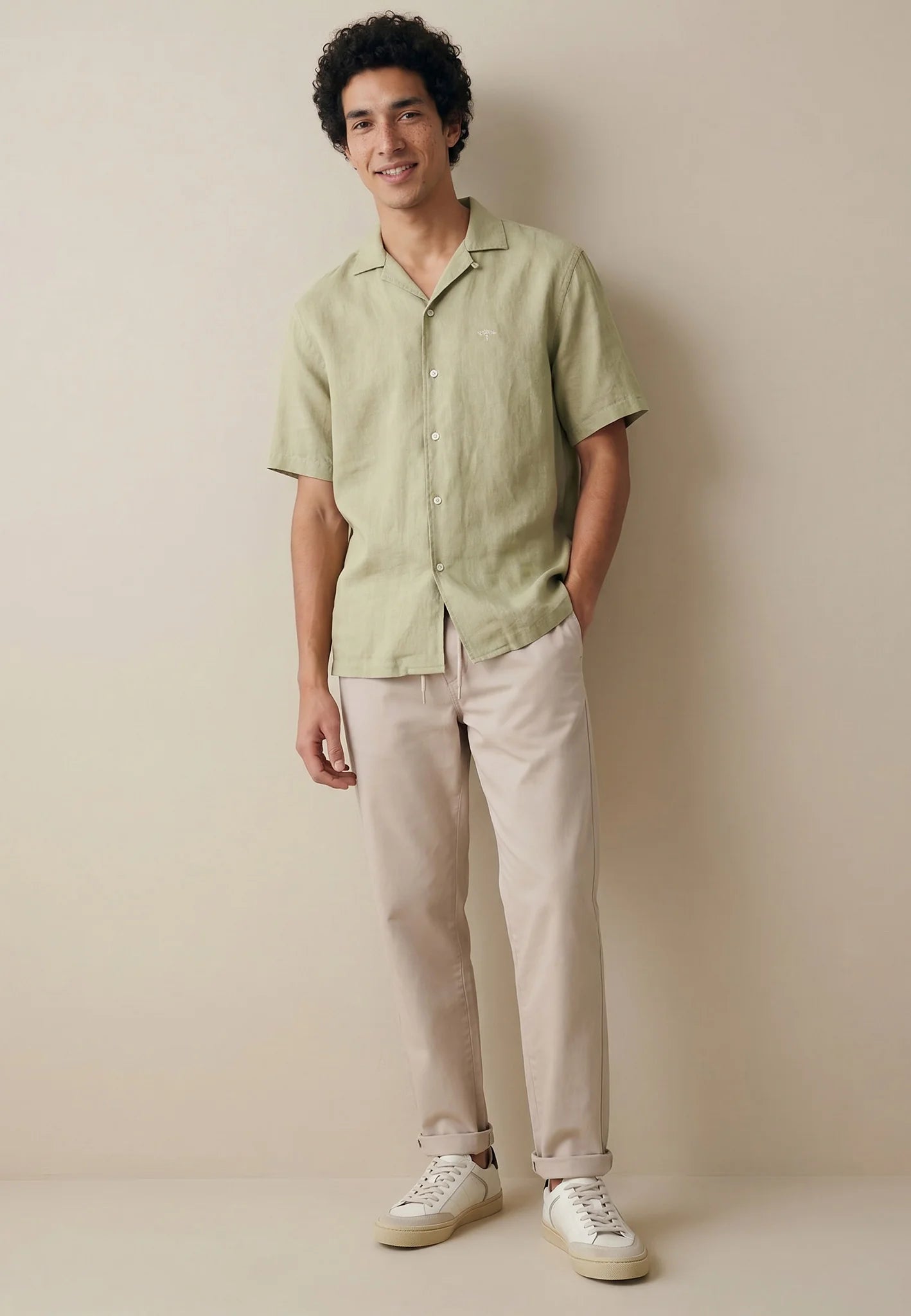 Man wearing a light green shirt and beige pants against a plain background