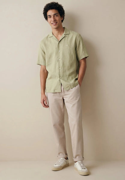 Man wearing a light green shirt and beige pants against a plain background