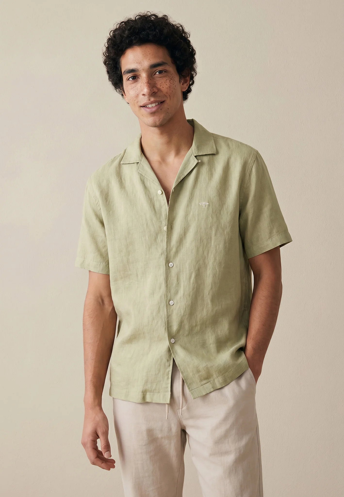 Man wearing a light green short-sleeve shirt and beige pants against a neutral background