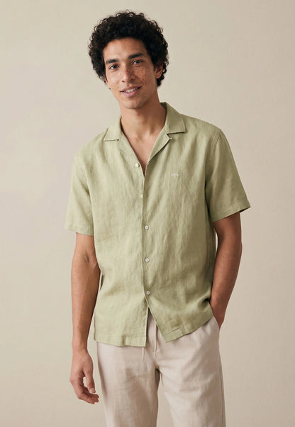 Man wearing a light green short-sleeve shirt and beige pants against a neutral background