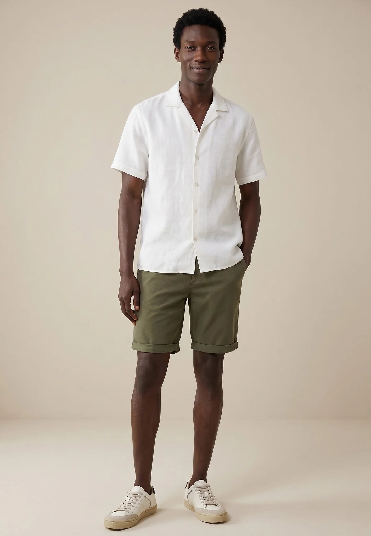 Man wearing a white shirt and green shorts against a beige background