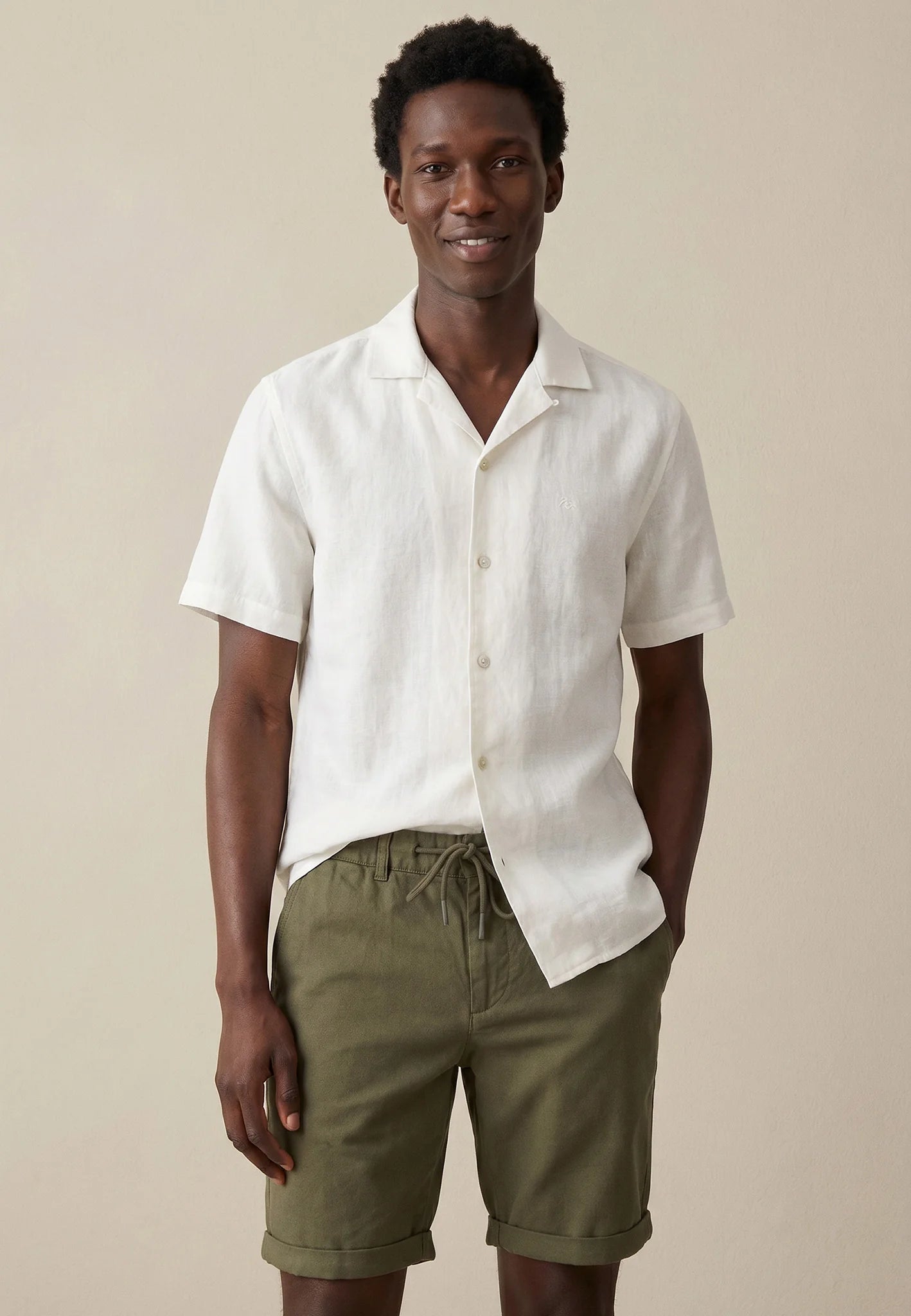 Man wearing a white linen shirt and green shorts against a beige background