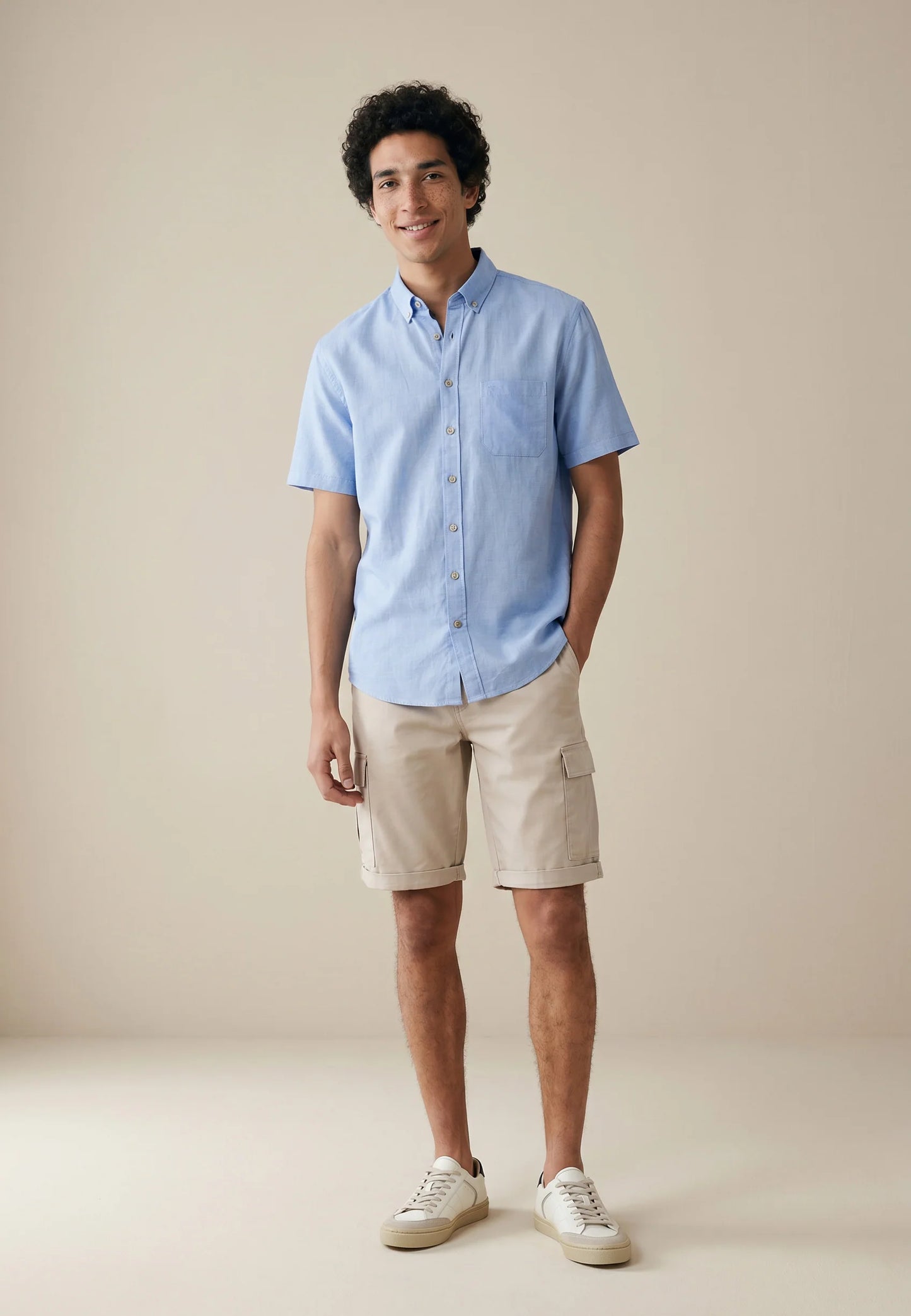 Man wearing a light blue shirt and beige shorts against a plain background