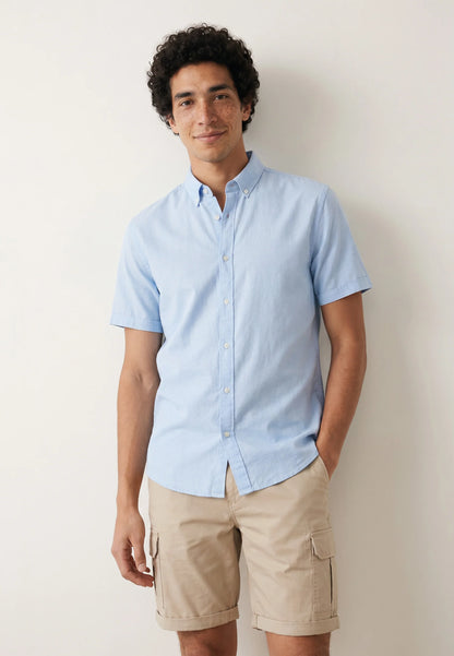Man wearing a light blue shirt and beige shorts against a plain background