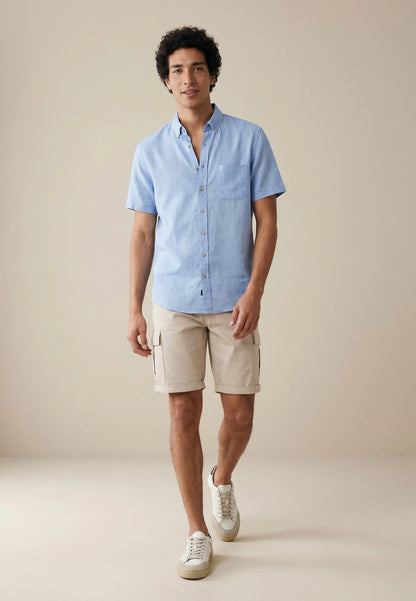 Man wearing a light blue button-up shirt and beige cargo shorts on a beige background