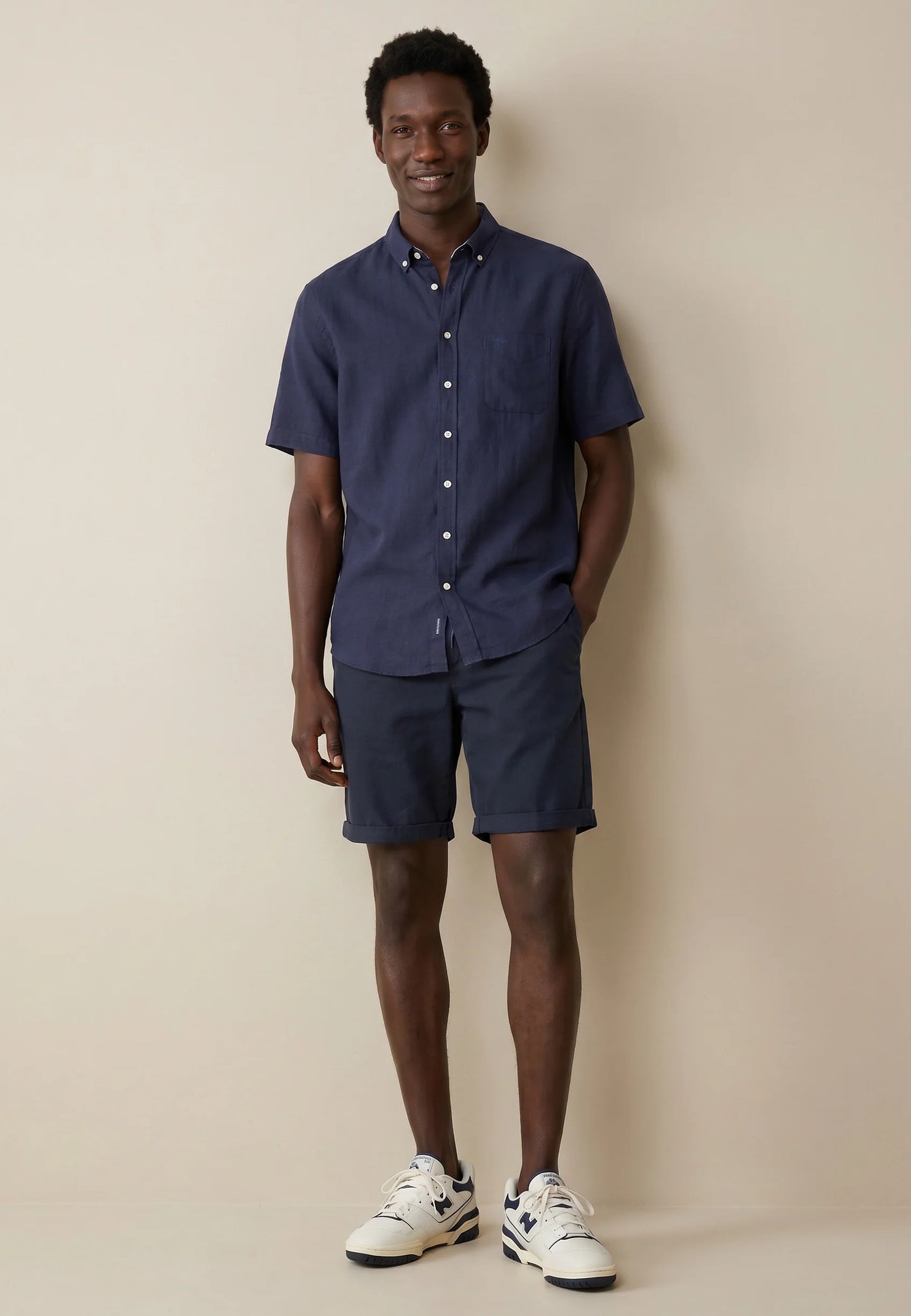 Man wearing a navy shirt and shorts with white sneakers against a beige background